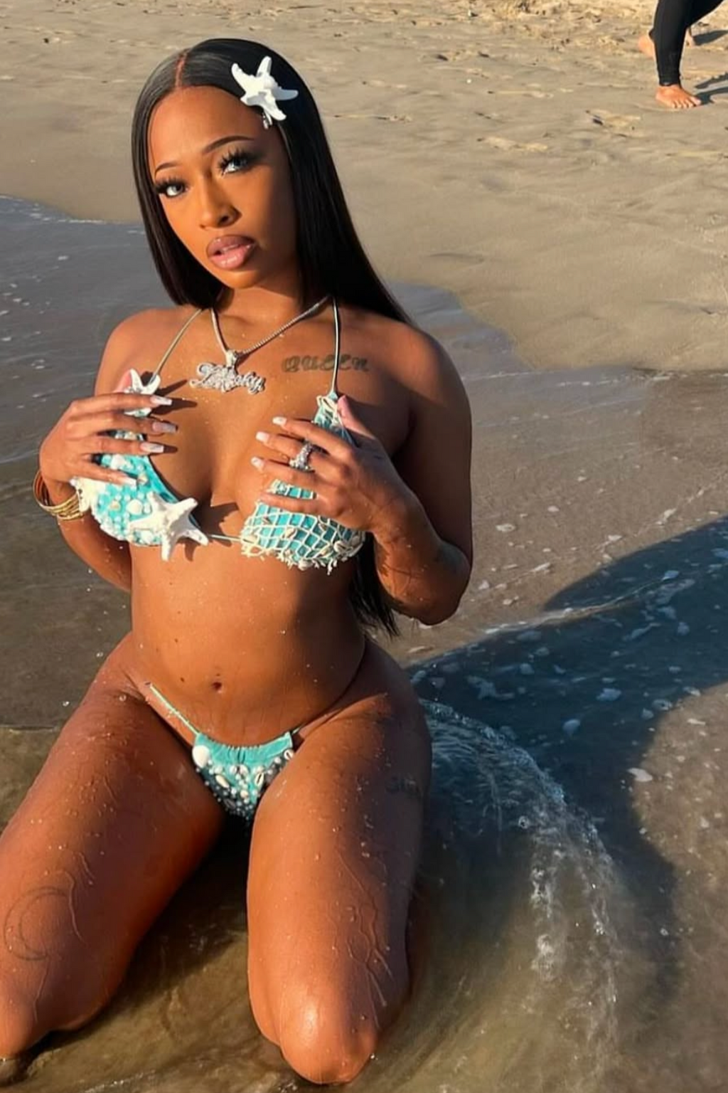 Woman in turquoise bikini sitting on a beach with a phone in hand.